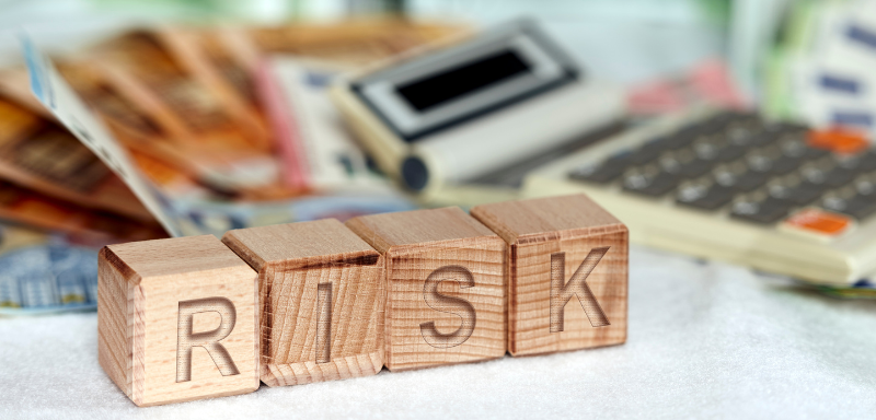 Bloques de madera escritos "risk", con calculadora y euros al fondo de la imagen.