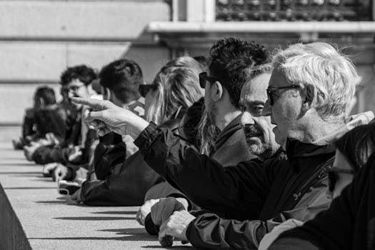 A group of people observing something with interest, highlighted in black and white, sitting in a row.
